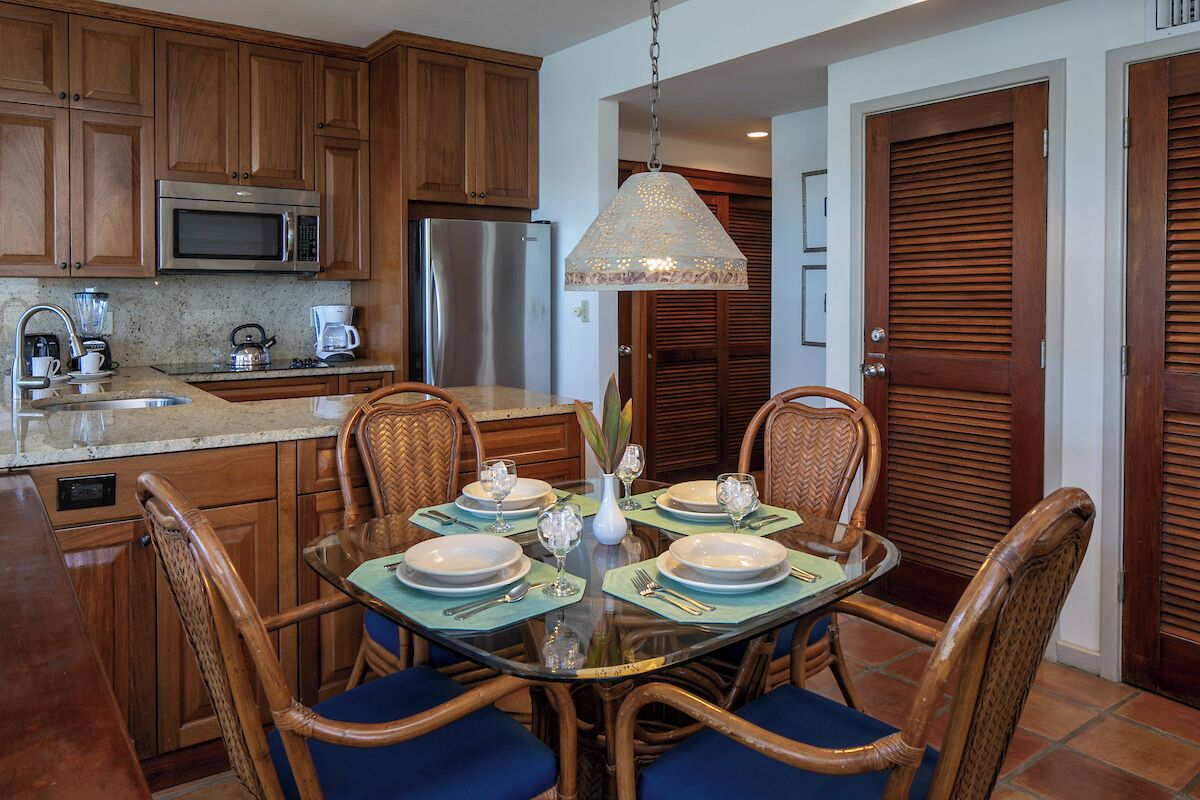 A dining area with a glass table, wicker chairs, and a hanging light fixture.