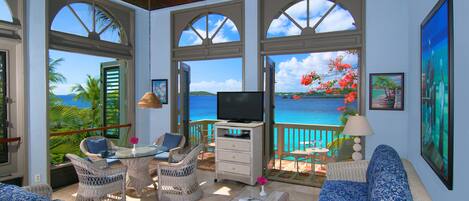 A spacious room with wicker furniture, a television, and large windows offering a view of the sea.
