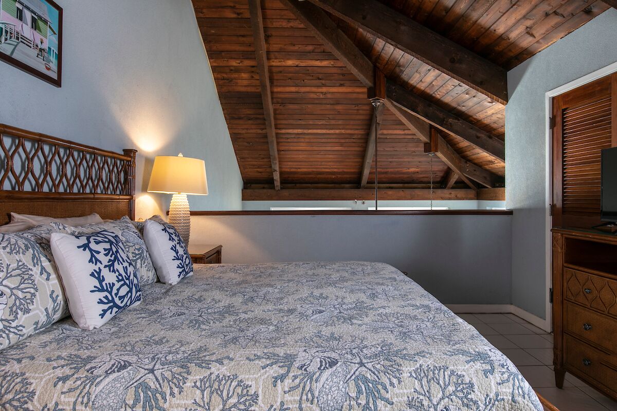 A bedroom with a large bed, wooden headboard, a nightstand with a lamp, and a wooden dresser.