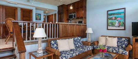 Una sala de estar con muebles de mimbre, una escalera y una cocina al fondo.