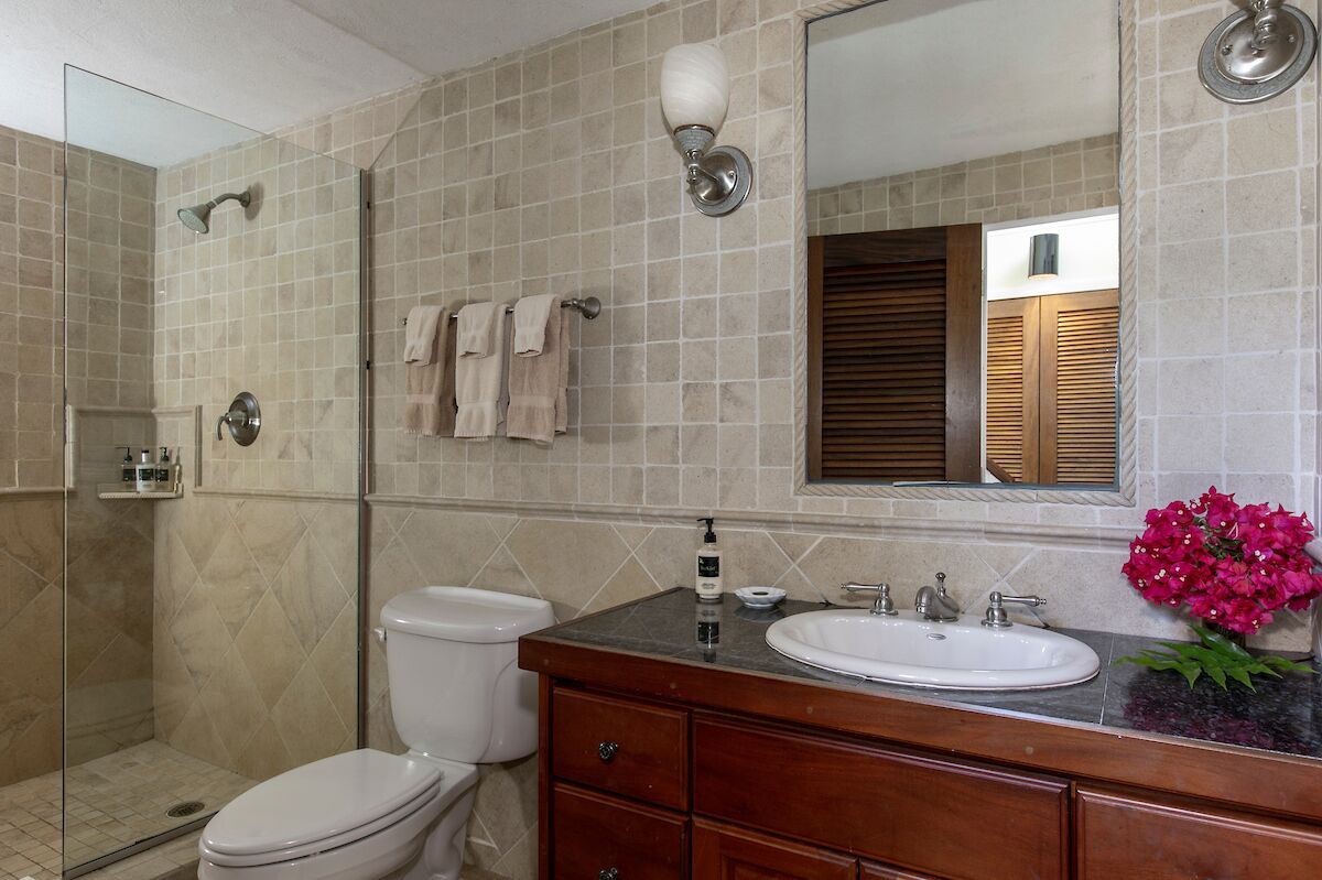 Un baño con cabina de ducha de vidrio, inodoro, lavabo con tocador y espejo.