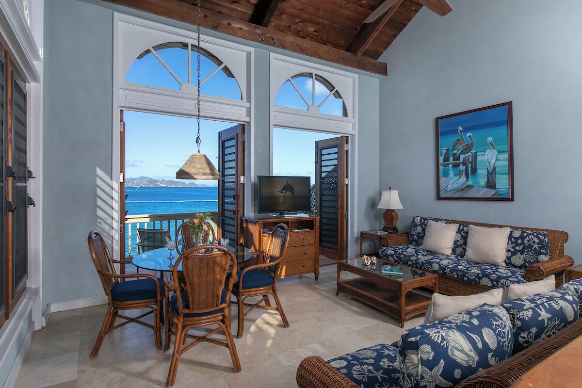 A spacious living area with a view of the ocean, a dining set, a sofa, and a television.