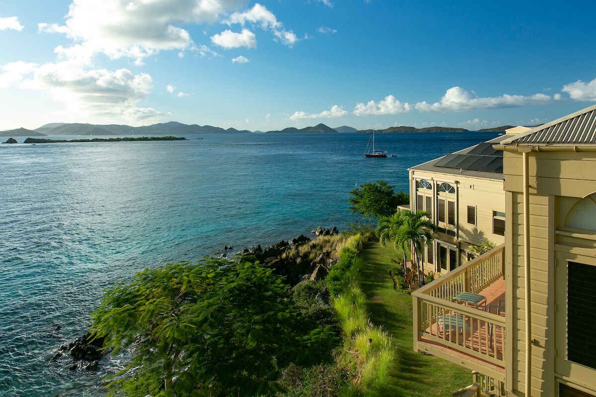 A coastal property with a view of the sea, a sailboat, and distant mountains.