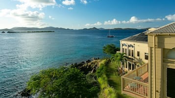 A coastal property with a view of the sea, a sailboat, and distant mountains.