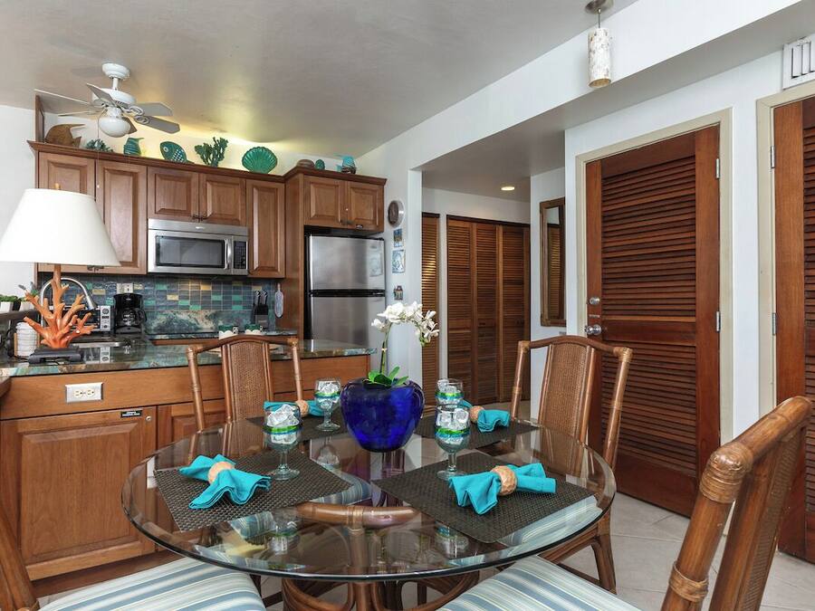 A modern kitchen with wooden cabinets, stainless steel appliances, and a dining area with a glass table and chairs.