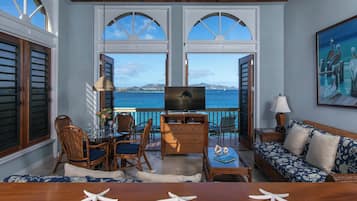 Um quarto acolhedor com televisão, móveis de madeira e vista para o mar através de portas em arco.