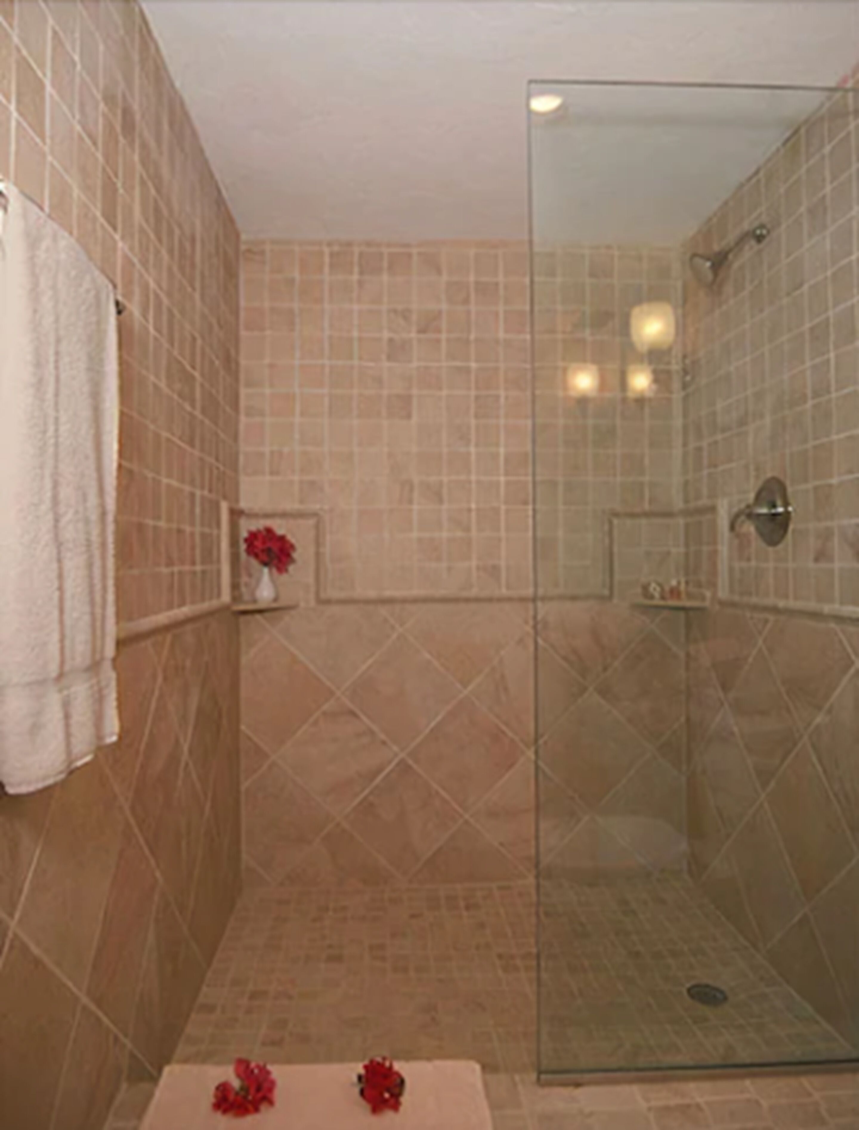 Ein Badezimmer mit beige gefliesten Wänden, einer Duschkabine aus Glas und einem weißen Handtuch an der Wand.