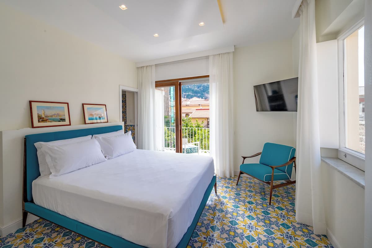 A hotel room with a bed, a chair, a TV, and a balcony with a view.