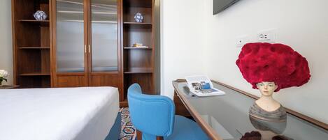 A hotel room with a bed, a blue chair, a wooden wardrobe, a flat-screen TV, and a red decorative item on the wall.