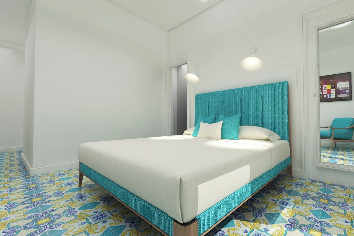 A bedroom with a bed, a teal headboard, and patterned floor tiles.