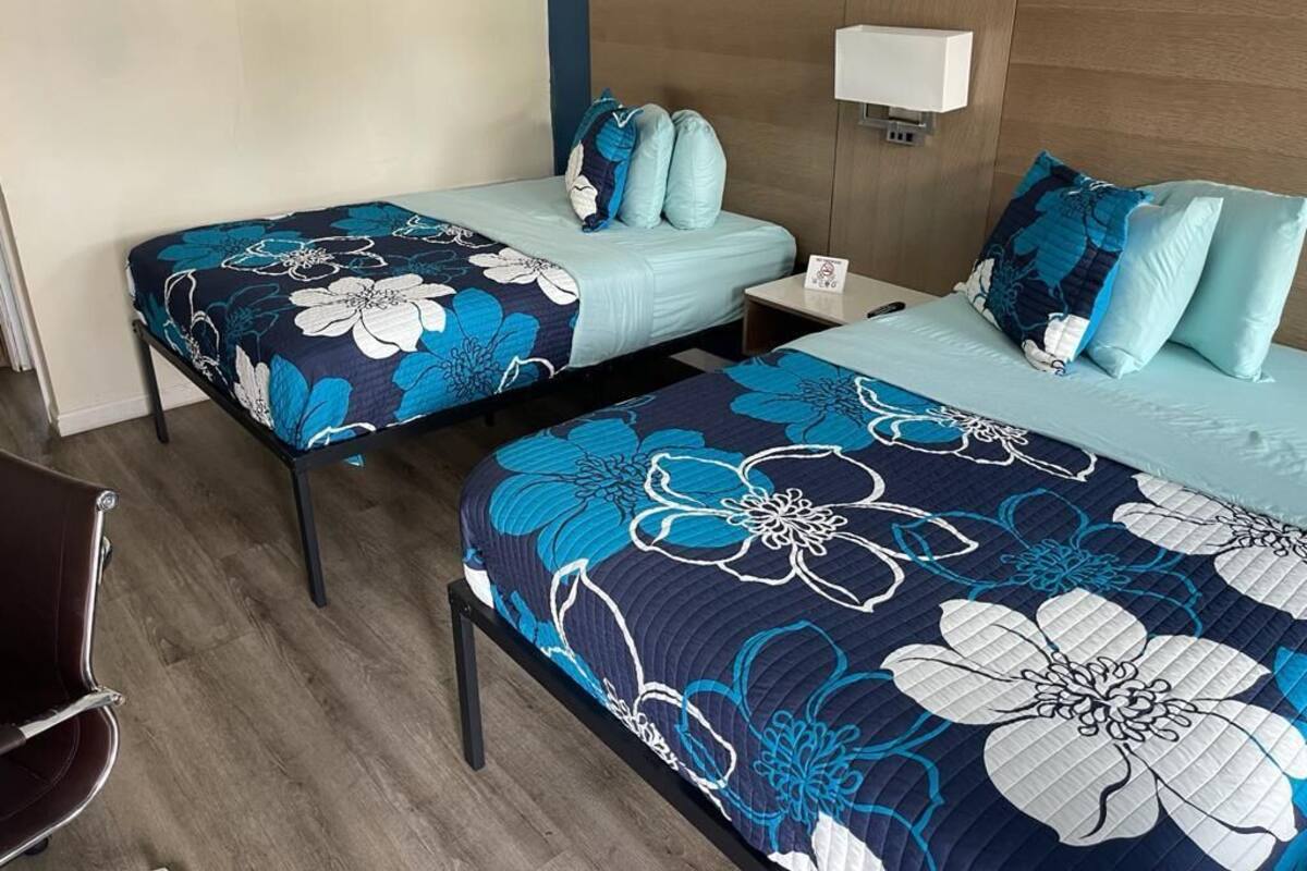Ett hotellrum med två sängar, där varje säng har sängkläder med blommönster, ett trägaveltavla, ett nattduksbord och en vägglampa.