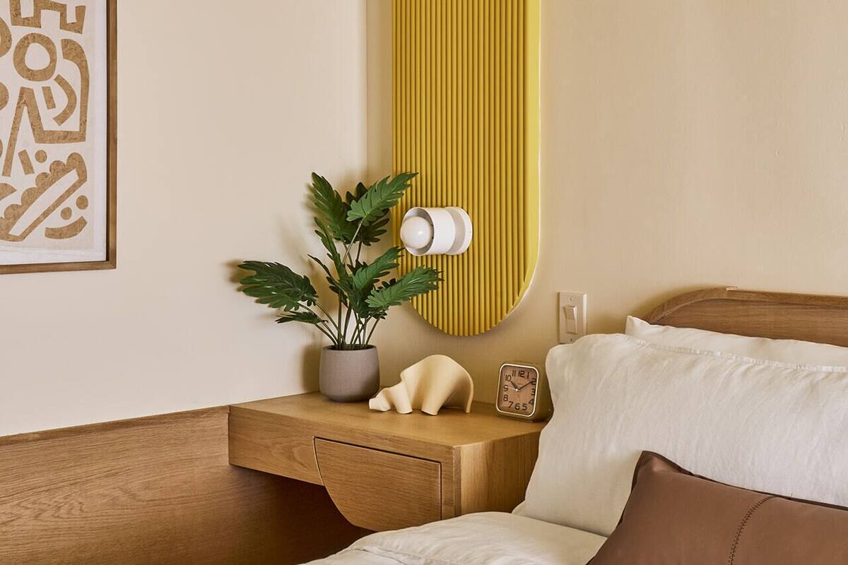 Ett välordnat hotellrum med en säng, ett sängbord och en väggmonterad lampa.