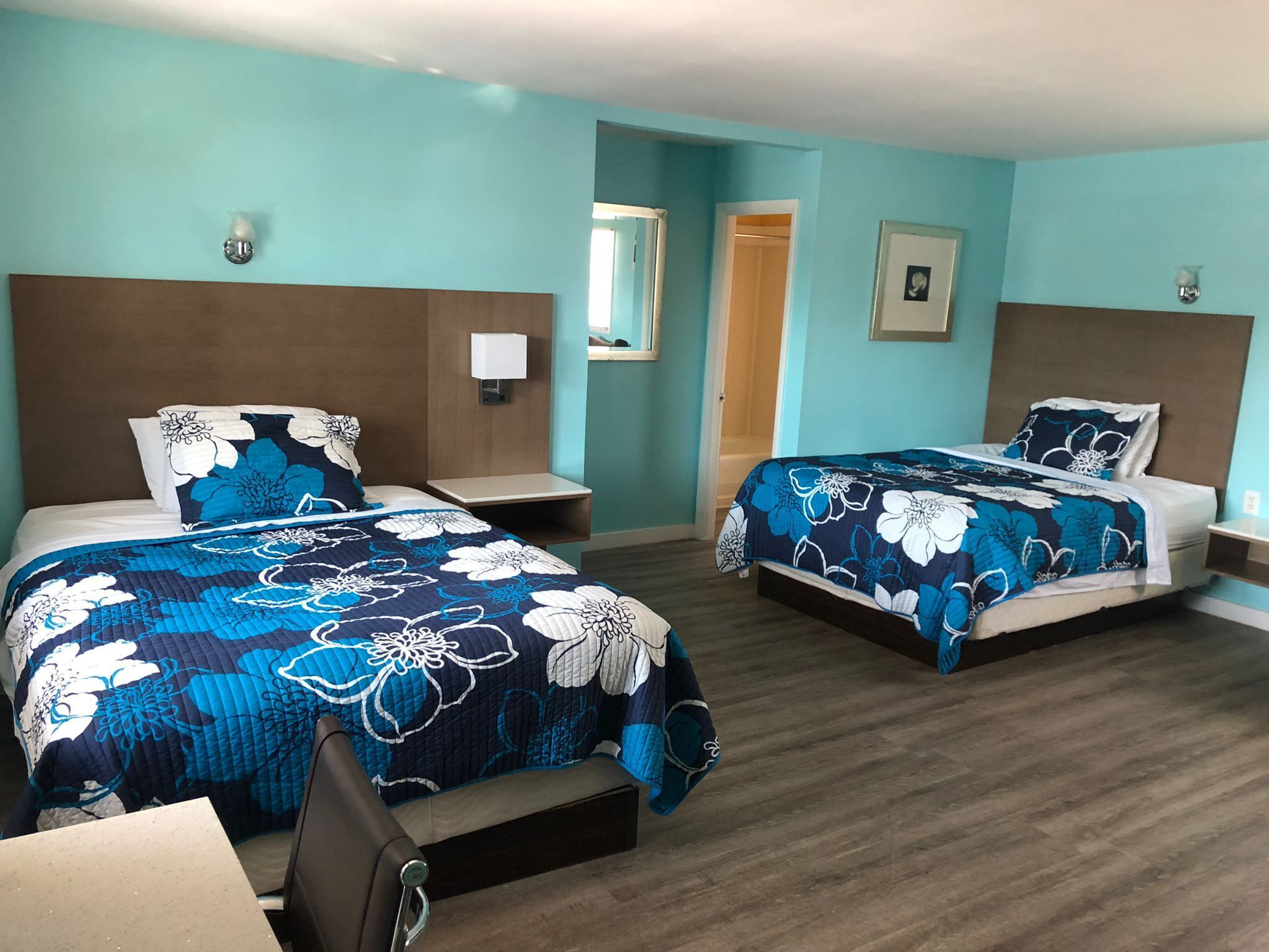 A hotel room with two beds, each with a floral-patterned bedspread, wooden headboards, and bedside tables with lamps.