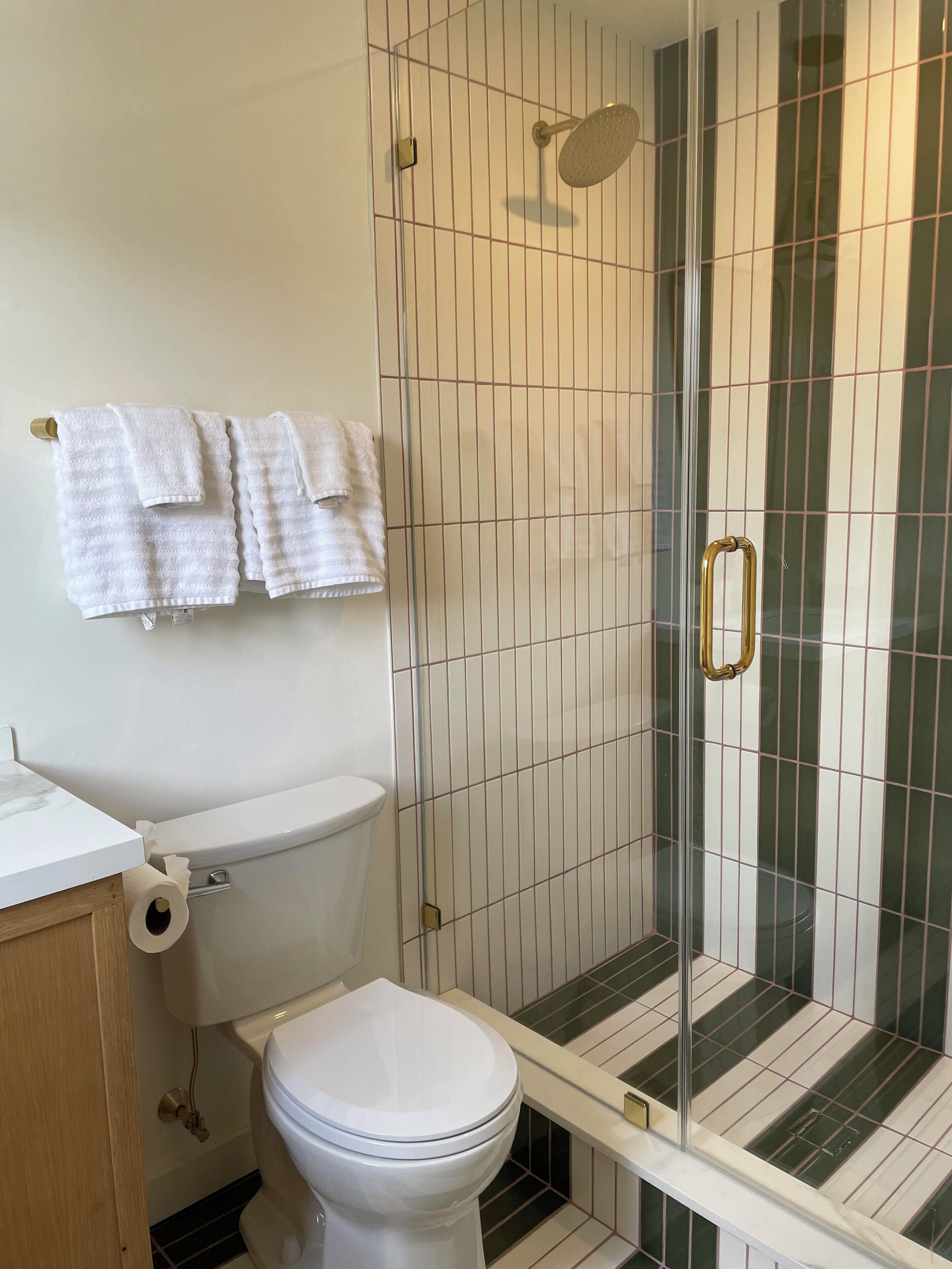 Un baño con inodoro, ducha con puerta de cristal y barra para toallas con toallas.