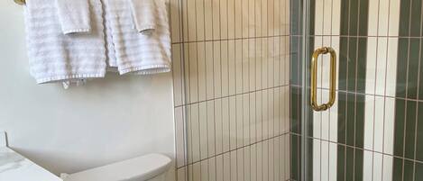 A bathroom with a toilet, a shower with a glass door, and a towel rack with towels.