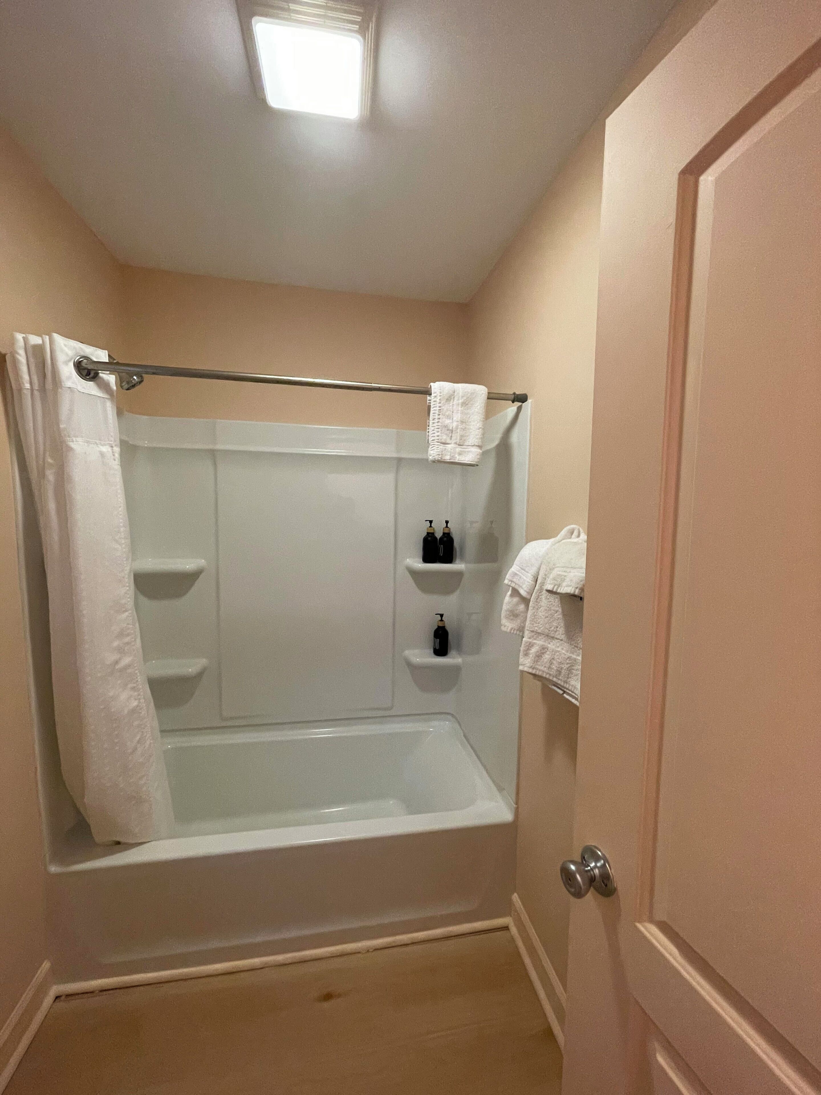 A small, single-person bathroom with a shower, a towel rack, and a shelf with toiletries.