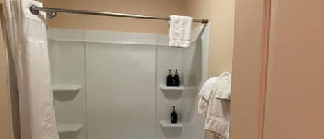 A small, single-person bathroom with a shower, a towel rack, and a shelf with toiletries.
