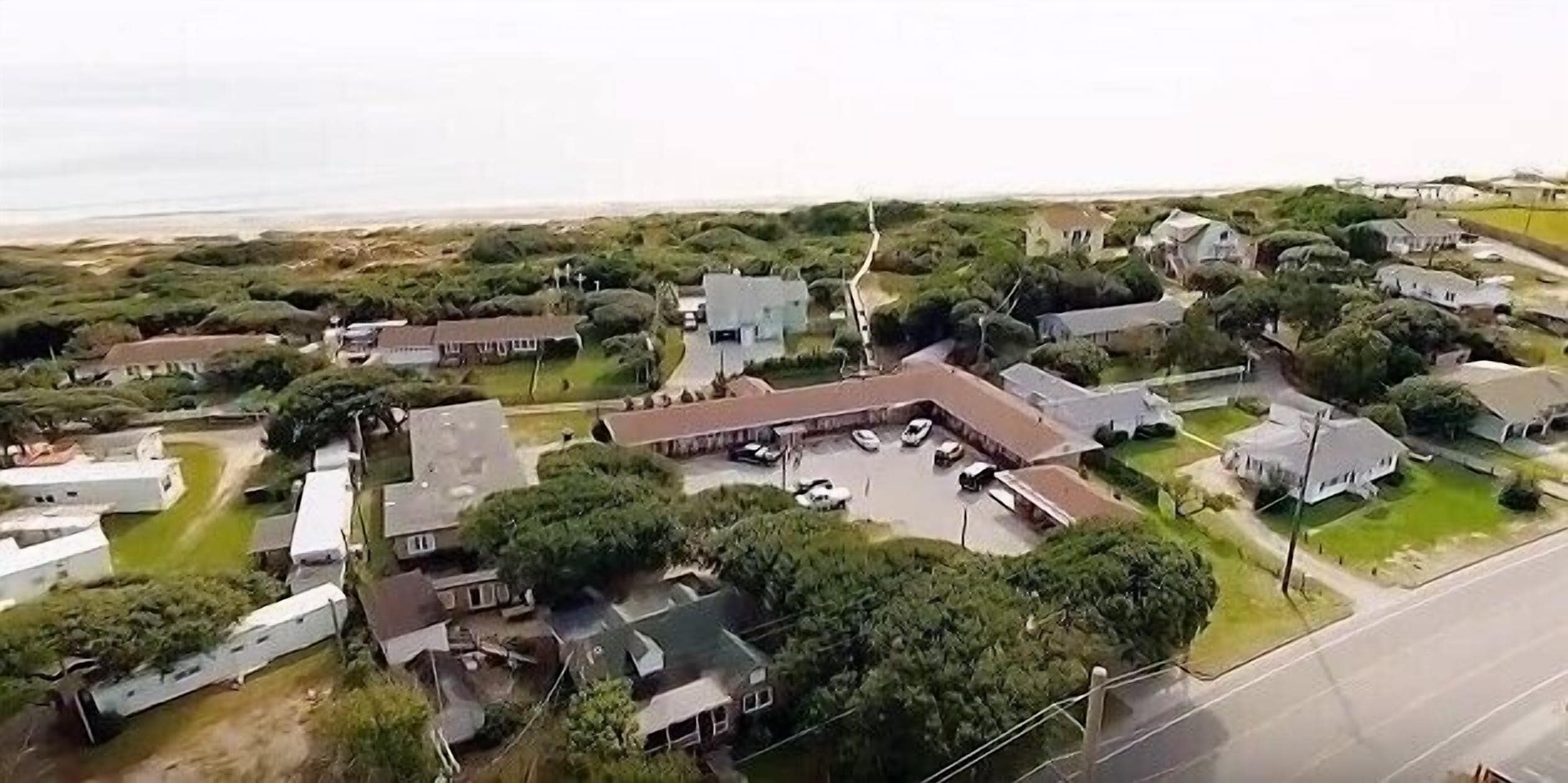 Vista aérea de uma área residencial com casas, um estacionamento e uma rua.