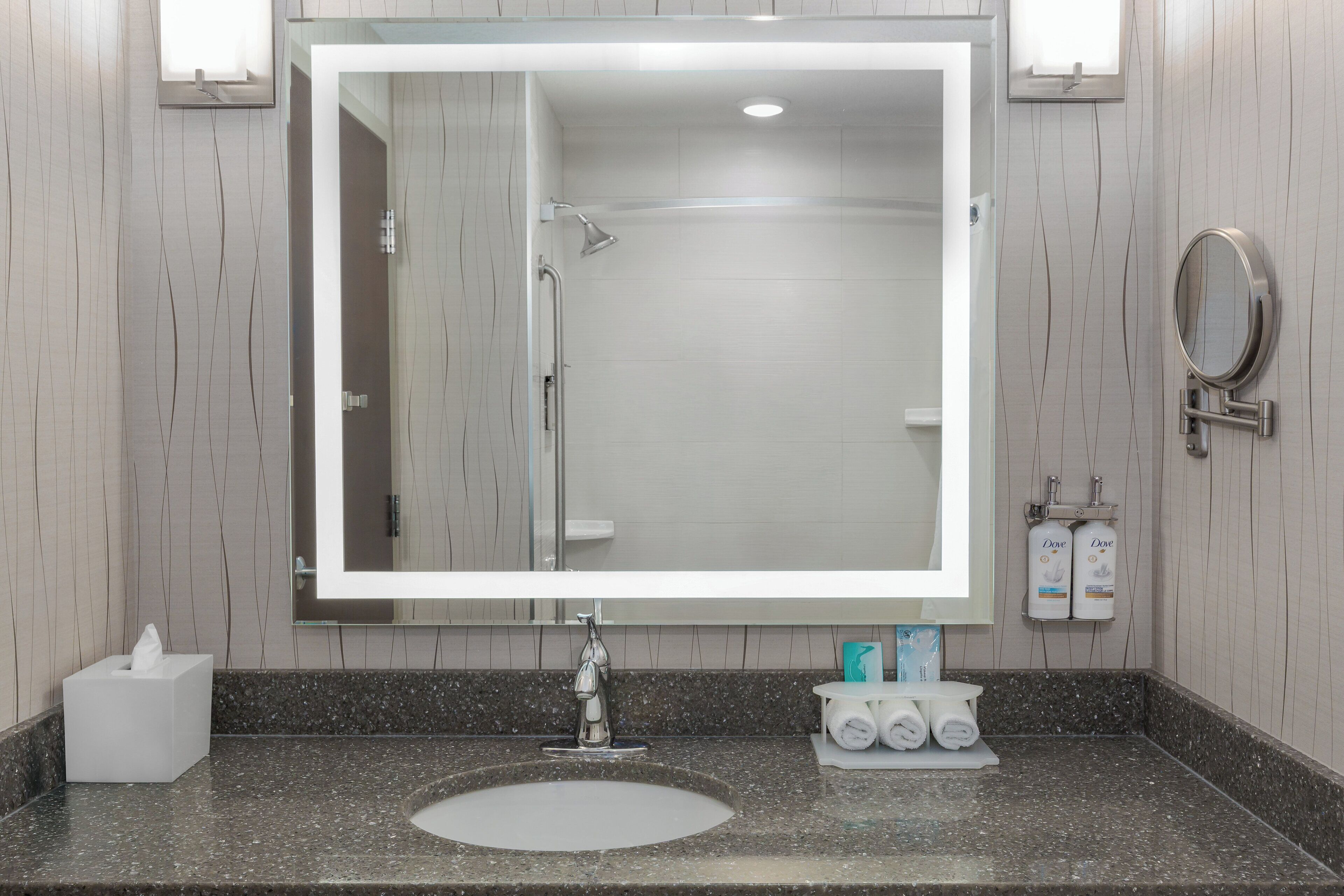 A modern bathroom with a large mirror, a sink, a shower, and toiletries.