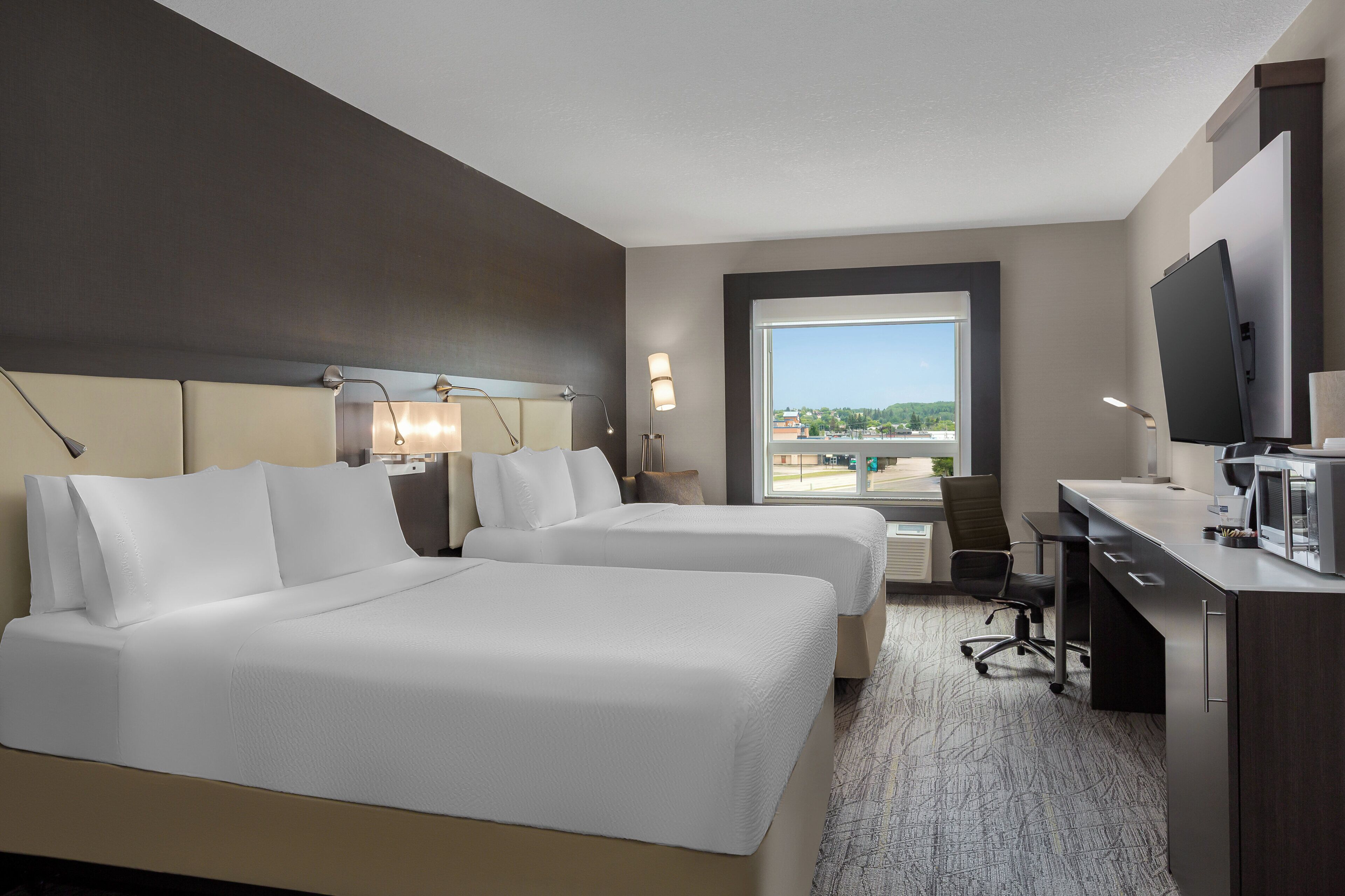 A hotel room with two beds, a desk, a chair, a television, and a large window with a view of the city.