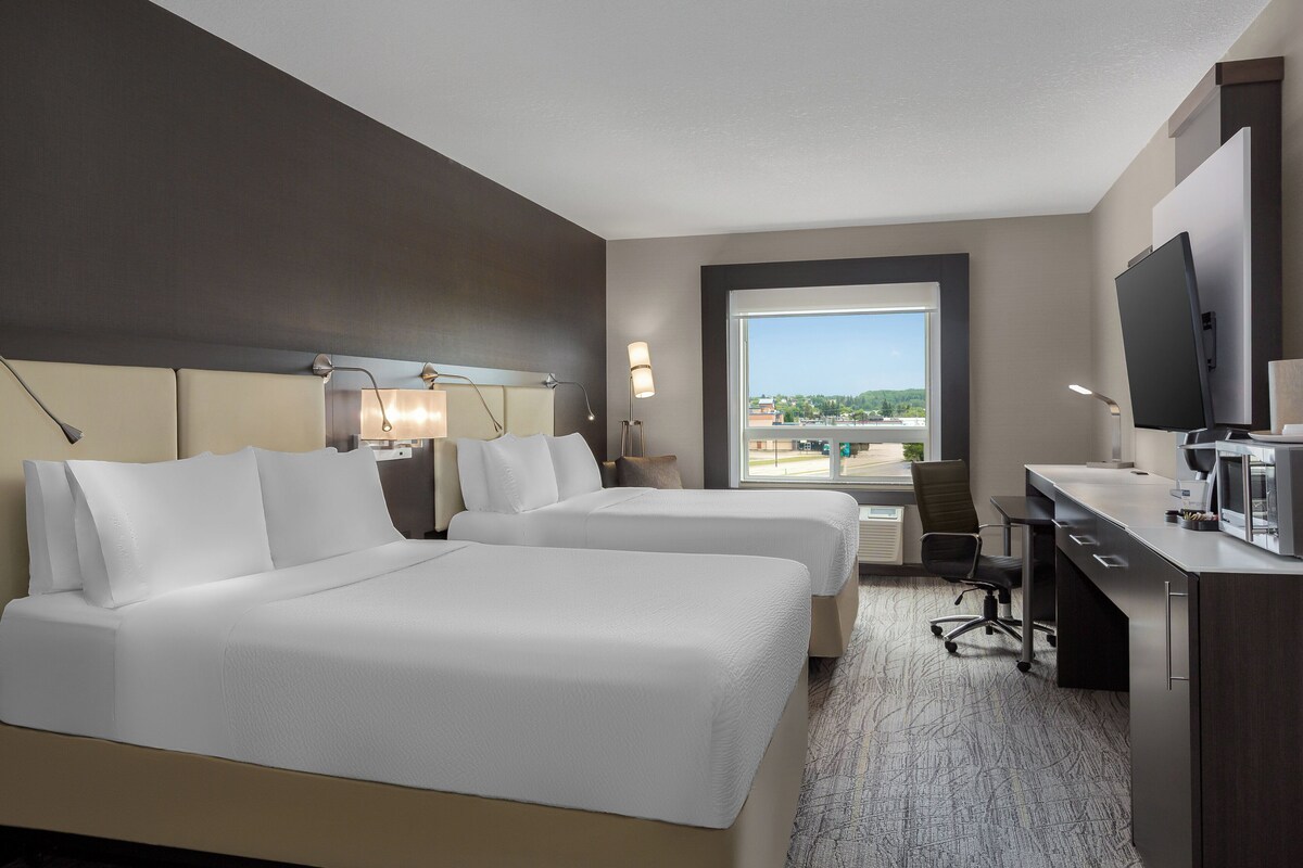 A hotel room with two beds, a desk, a chair, a television, and a large window with a view of the city.