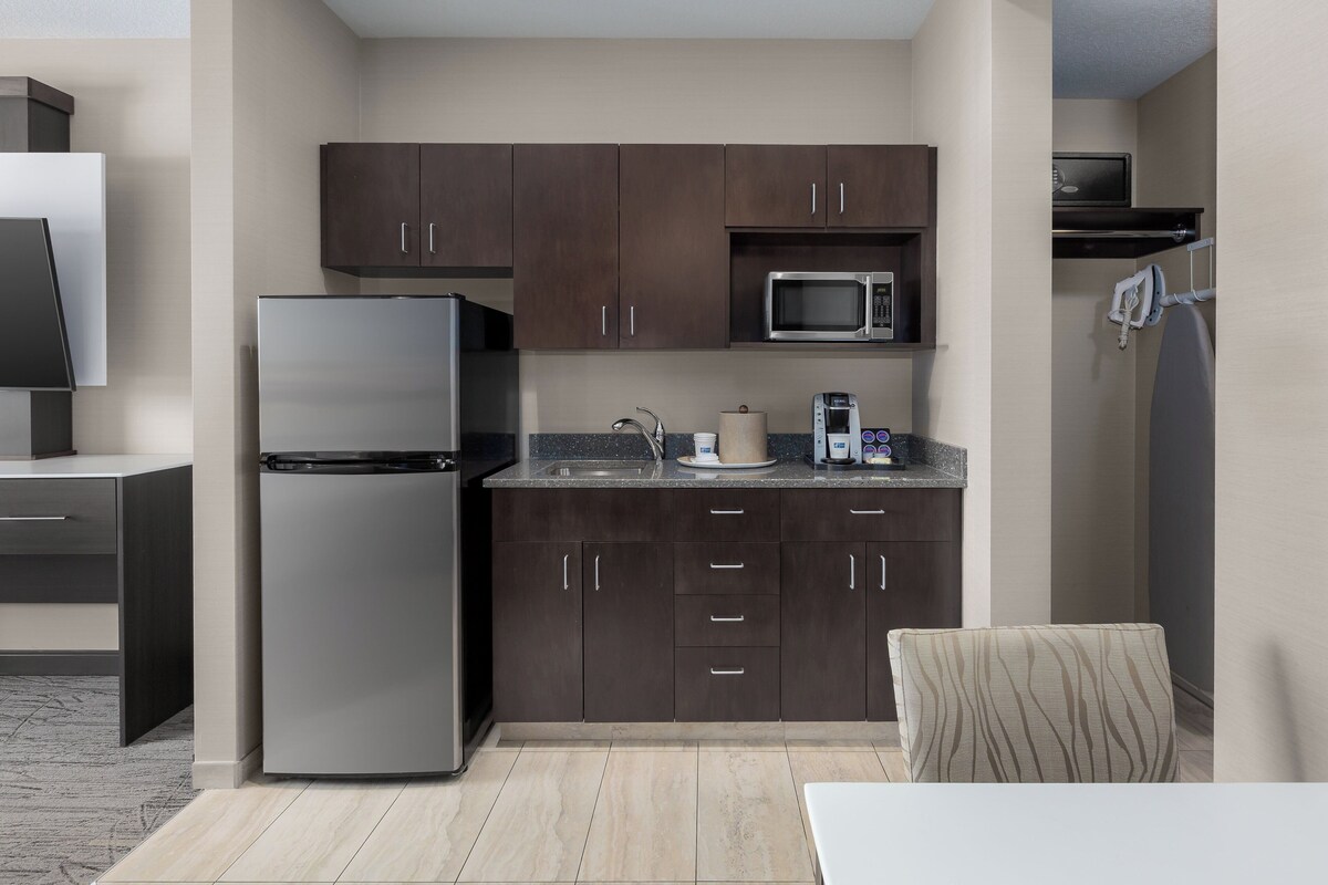 A modern kitchen with dark cabinets, a stainless steel refrigerator, a microwave, and a sink.