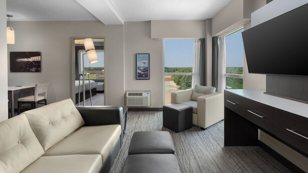 Quarto de hotel moderno com sofá, mesa pequena, TV e varanda com vista.