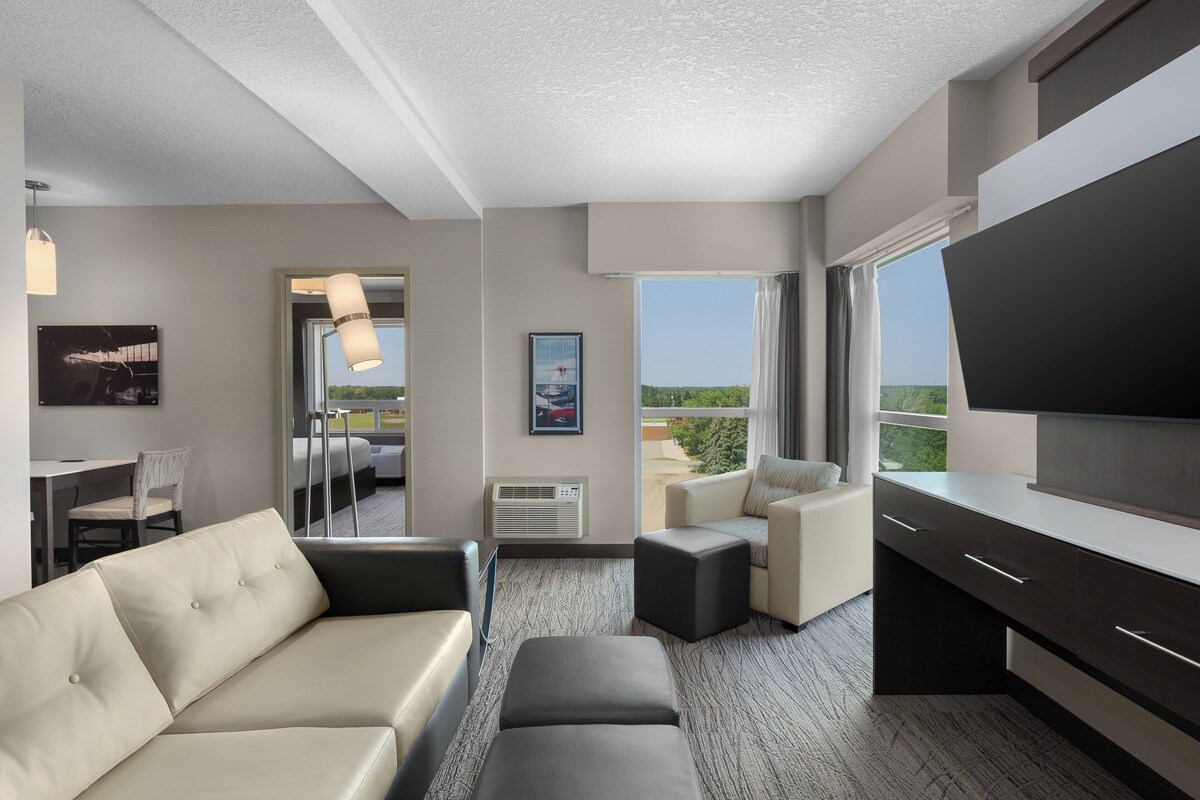 A modern hotel room with a sofa, a small table, a TV, and a balcony with a view.