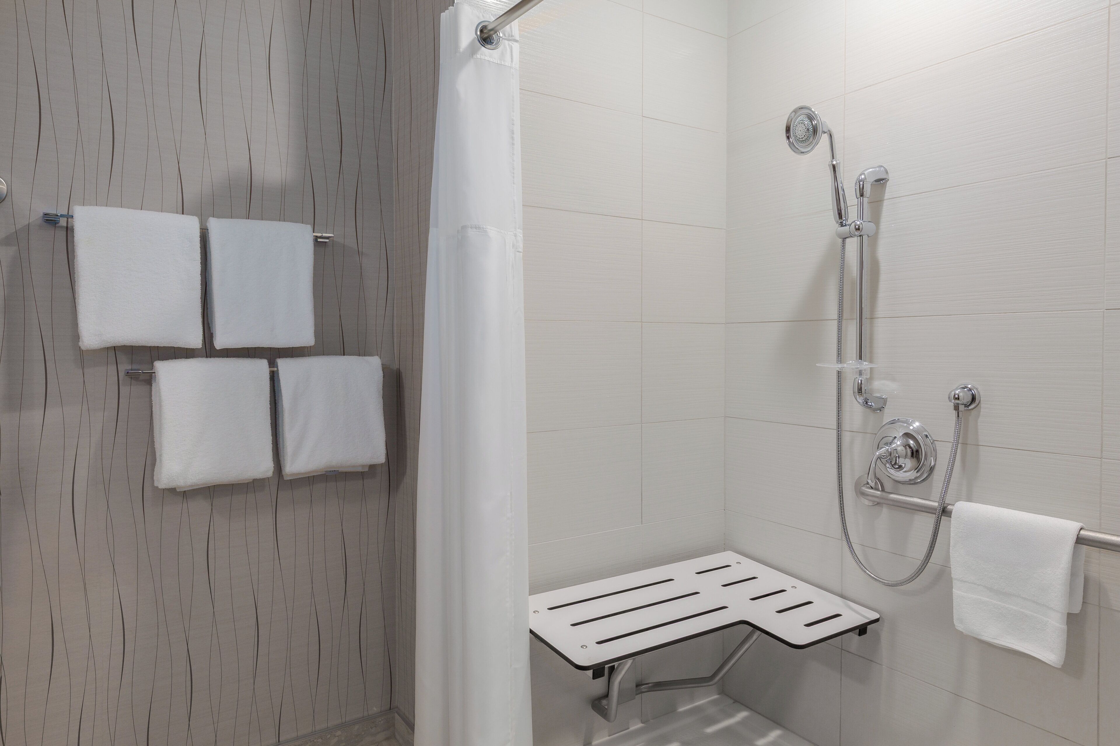 A modern shower area with a handheld showerhead, a towel rack with four towels, and a shower seat.
