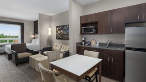 Quarto de hotel moderno com cozinha compacta, área de refeições e espaço de estar com vista para o exterior.