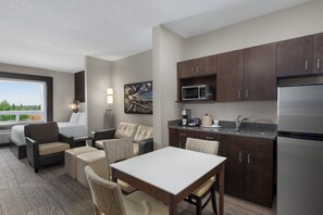 A modern hotel room with a kitchenette, a dining area, and a seating area with a view of the outdoors. - Holiday Inn Express & Suites Cold Lake by IHG (Cold Lake)