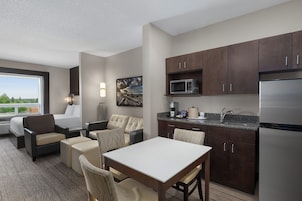 Una habitación de hotel moderna con kitchenette, comedor y zona de estar con vistas al exterior.