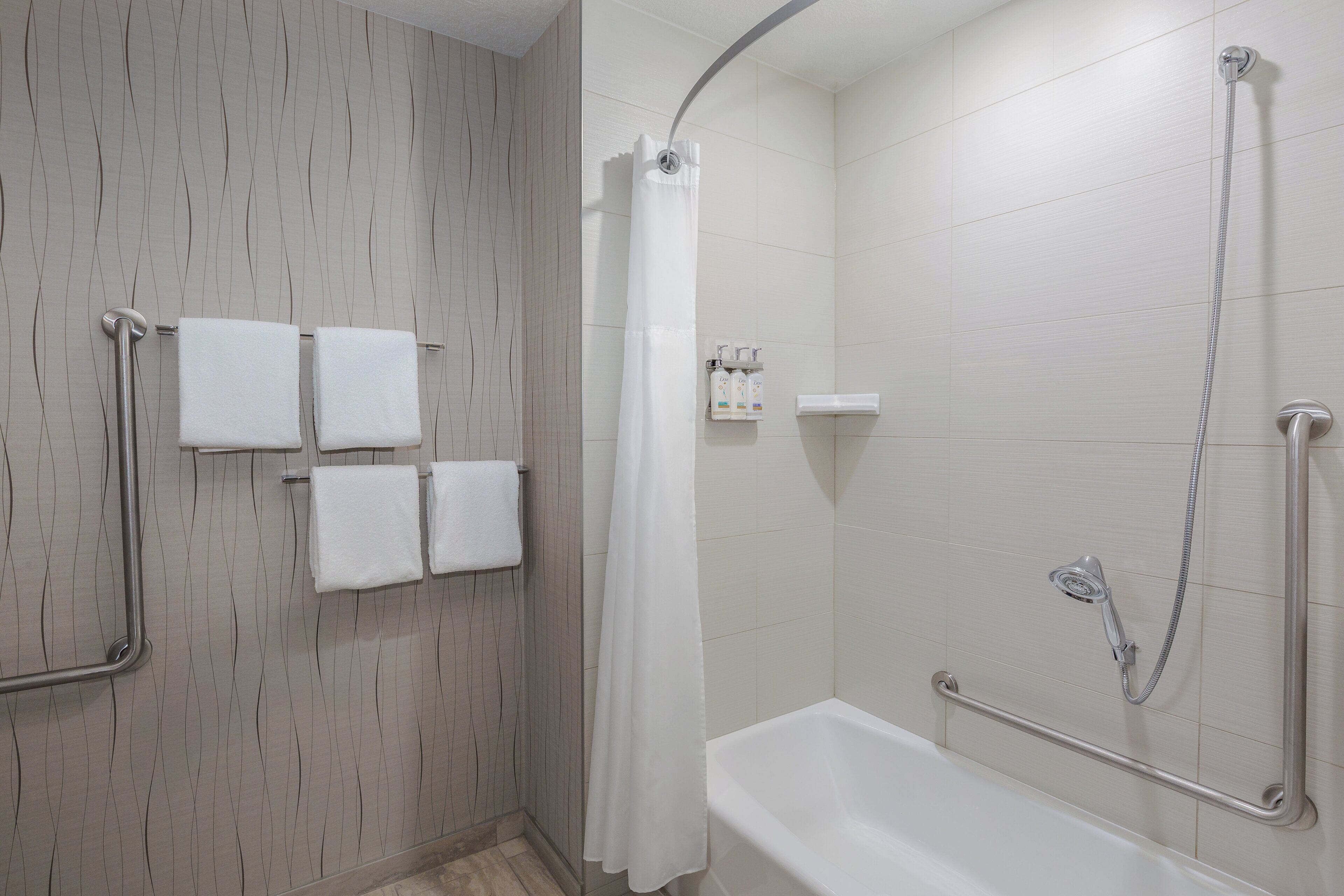 A bathroom with a shower, a bathtub, and handrails.