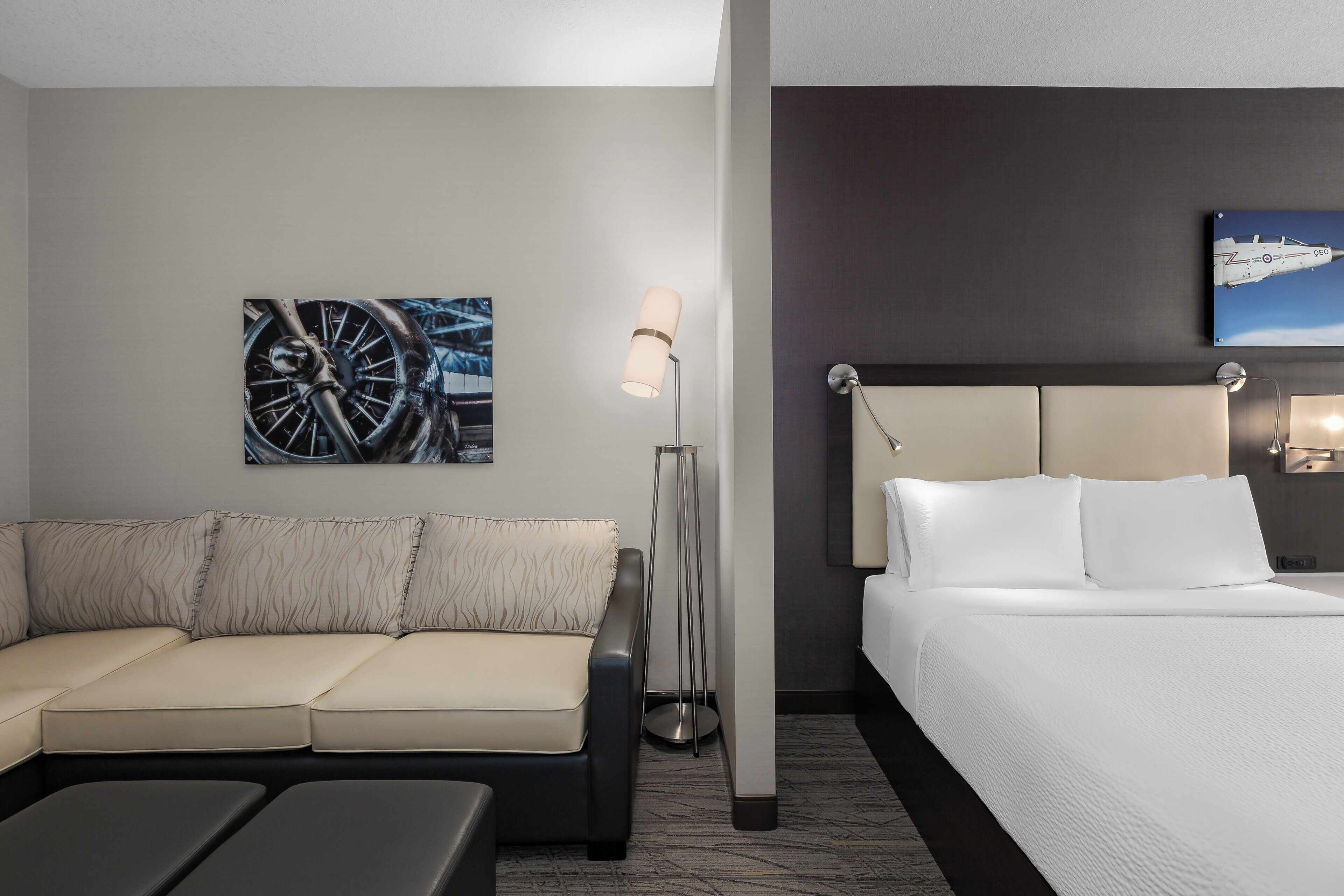 Habitación de hotel con cama, sofá, lámpara de pie y obras de arte en las paredes.