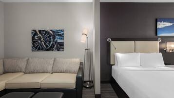 Habitación de hotel con cama, sofá, lámpara de pie y obras de arte en las paredes.