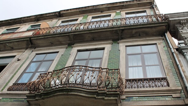 Un edificio de varios pisos con balcones de hierro ornamentados y ventanas amplias.
