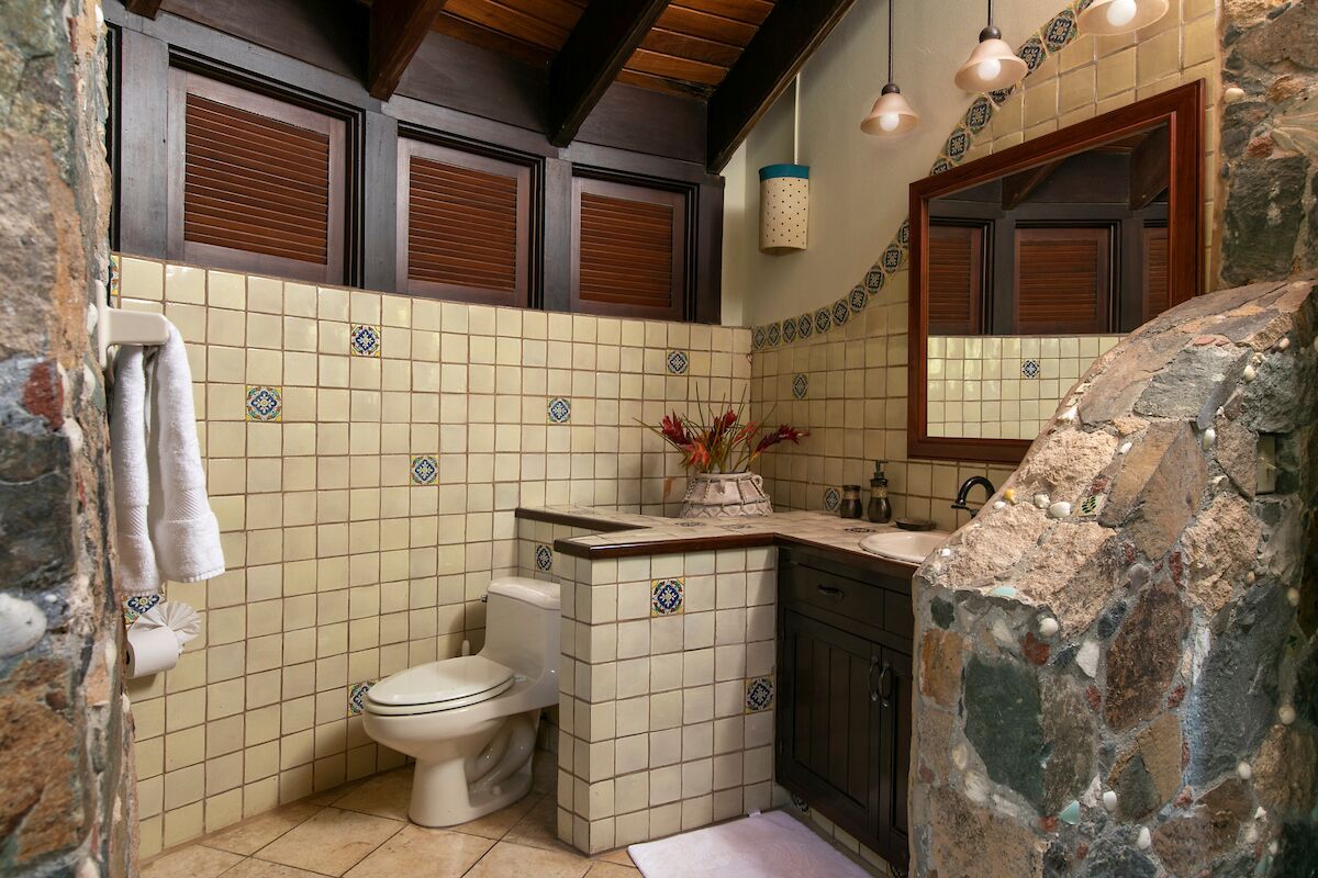 A bathroom with a toilet, sink, and mirror. There are towels hanging on the wall and a vase with flowers on the counter.