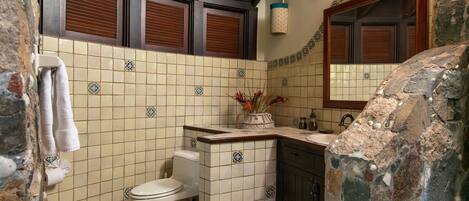 A bathroom with a toilet, sink, and mirror. There are towels hanging on the wall and a vase with flowers on the counter.