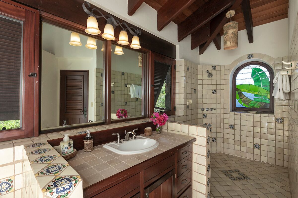 A bathroom with a large mirror, multiple light fixtures, a sink, and a shower area with decorative tiles.