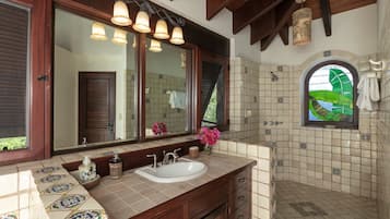 Un baño con un espejo grande, varias luminarias, un lavamanos y una zona de ducha con azulejos decorativos.