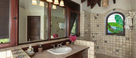 A bathroom with a large mirror, multiple light fixtures, a sink, and a shower area with decorative tiles.
