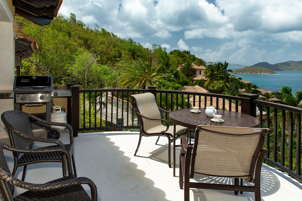 A balcony with wicker chairs, a table, and a grill.