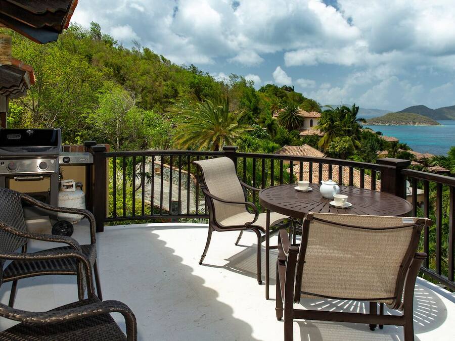 A balcony with wicker chairs, a table, and a grill.
