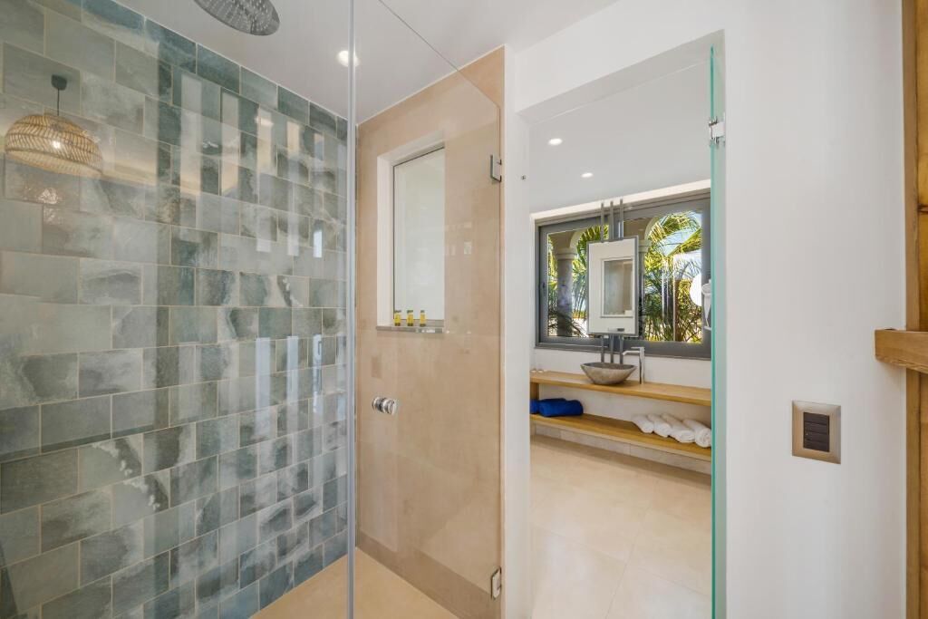 A modern bathroom with a glass shower enclosure, a large mirror, and a view of the outdoors.