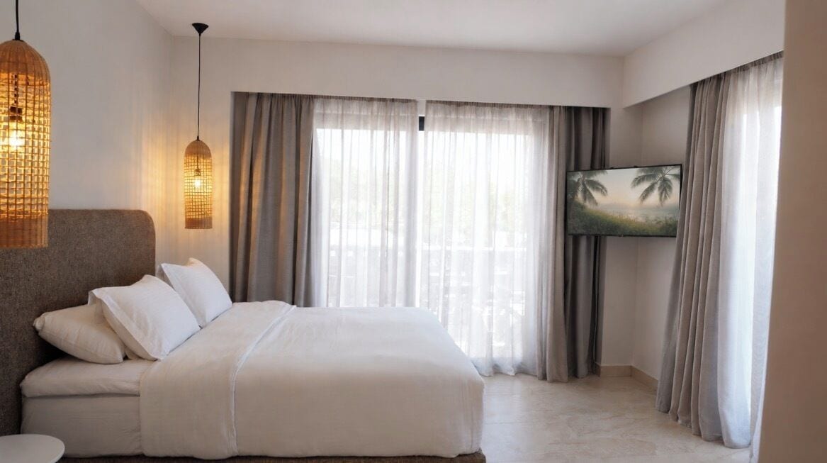 A hotel room with a bed, curtains, a television, and a wall-mounted picture.