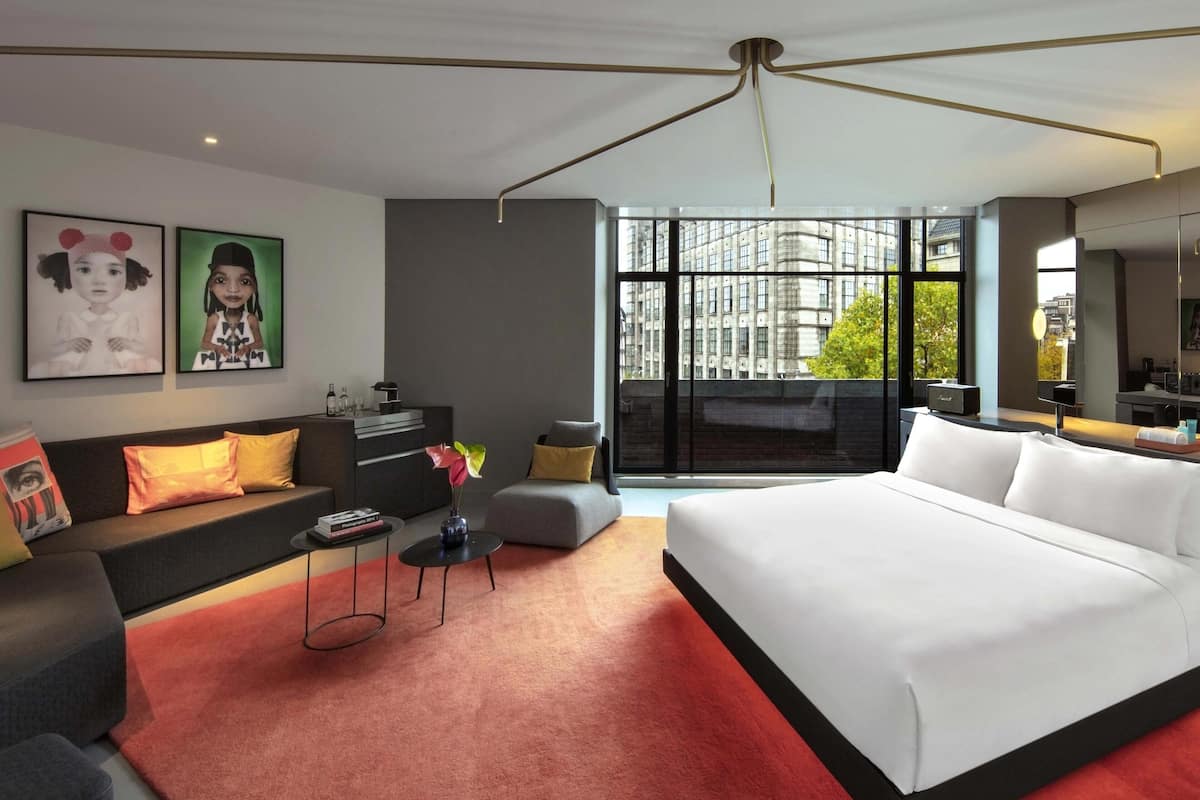A modern hotel room with a large bed, a sofa, a small table with a vase, and artwork on the wall.