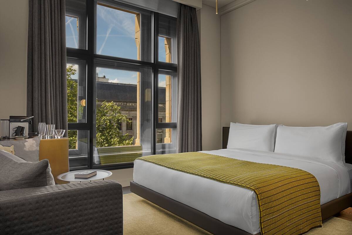 A hotel room with a large bed, a sofa, a small table, and a window with curtains.