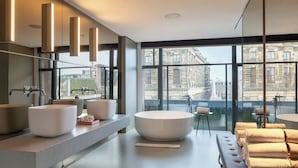 A modern bathroom with large windows, a large bathtub, and a vanity with multiple sinks. - W Amsterdam (Amsterdam)