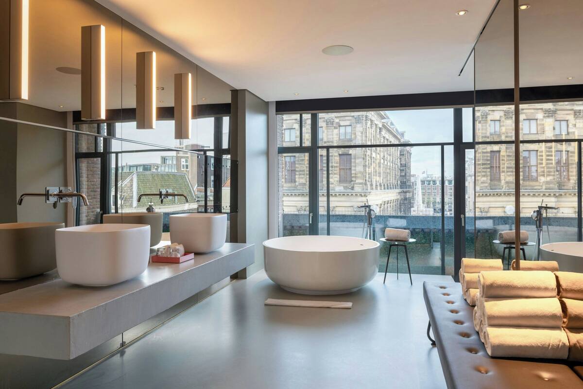 A modern bathroom with large windows, a large bathtub, and a vanity with multiple sinks.