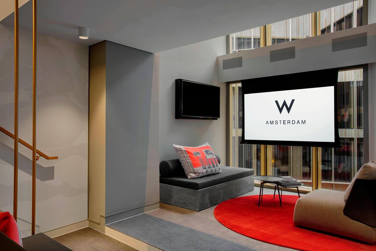 A modern living room with a grey sofa, a red rug, and a flat-screen TV displaying "AMSTERDAM".